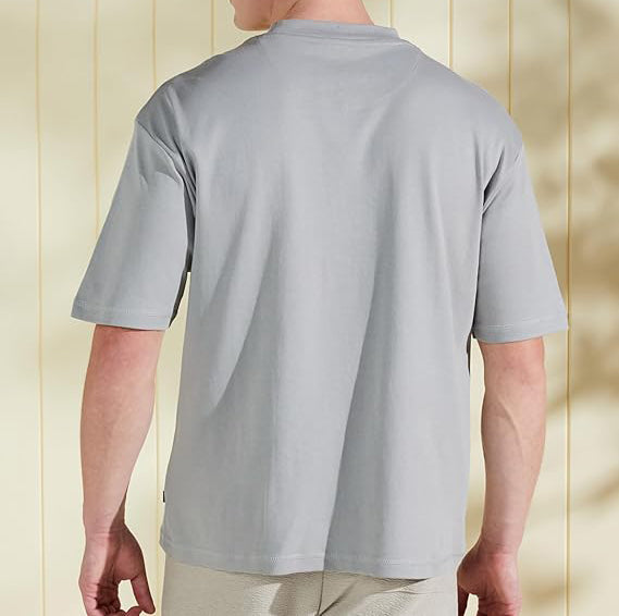 Person wearing a plain gray t-shirt against a light wooden panel background